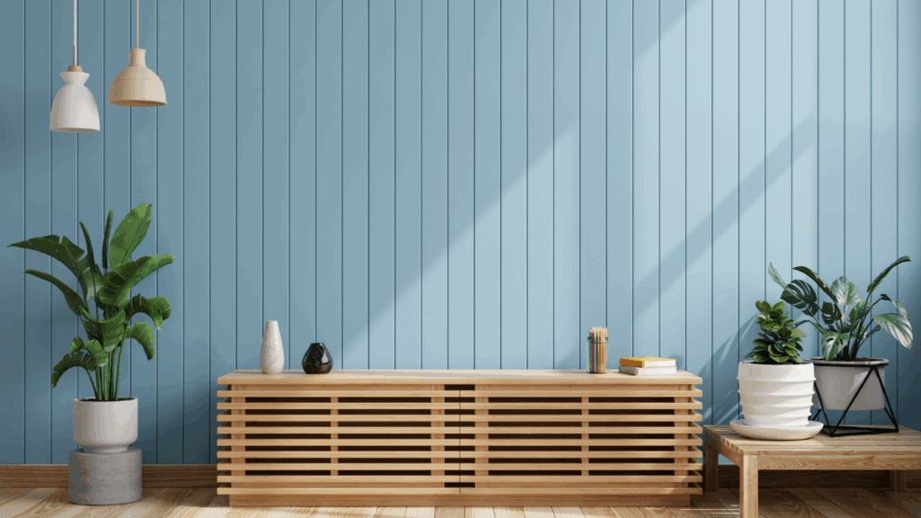 Jasne wnętrze z niebieską, pionową boazerią, drewnianą komodą, zielonymi roślinami