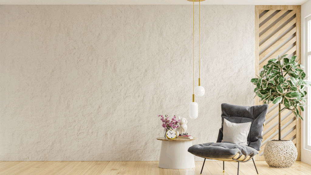 Minimalistyczne wnętrze z szarą leżanką, stolikiem i dużą rośliną na tle beżowej ściany.