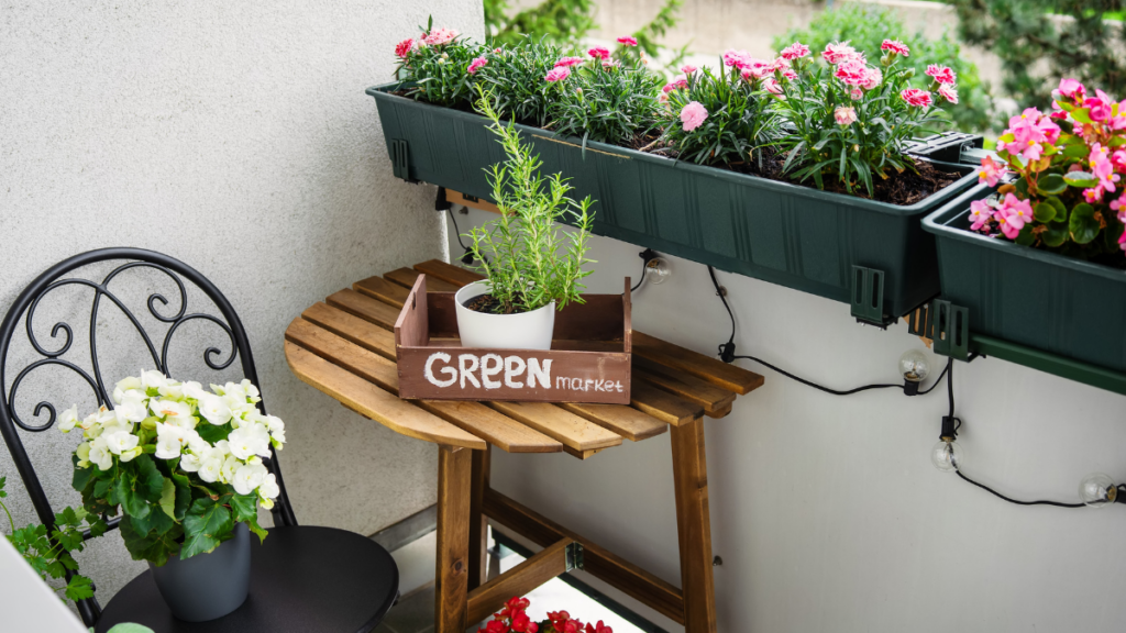 Mały balkon w bloku z drewnianym stolikiem, krzesłem oraz skrzynkami z kwiatami