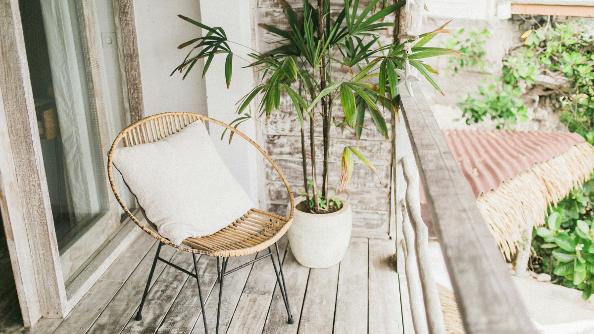 Balkon z drewnianą nawierzchnią, rattanowym krzesłem i rośliną w donicy